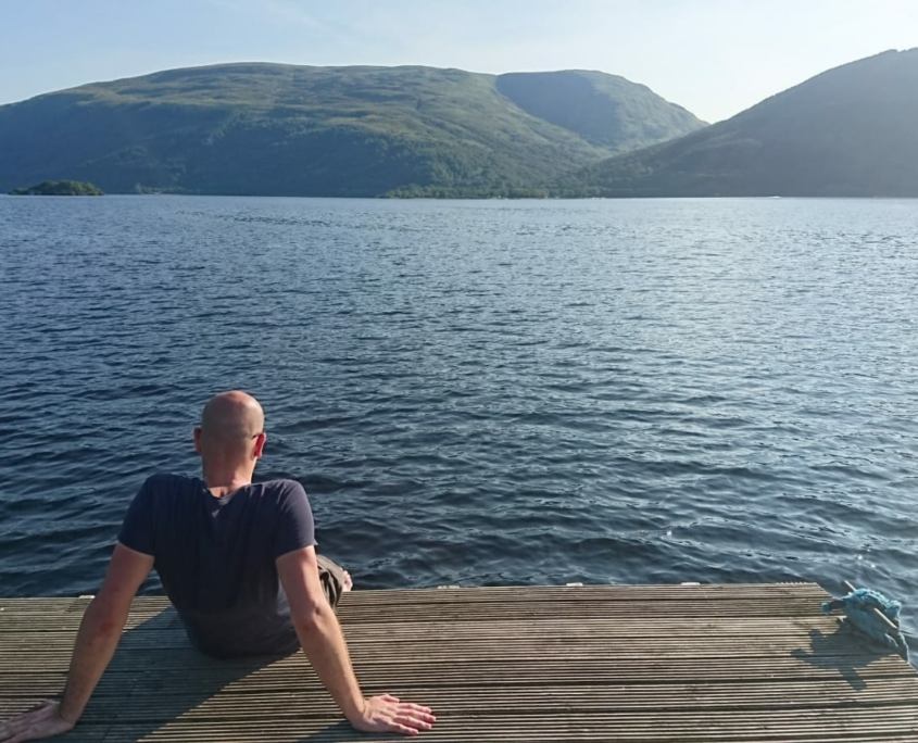 Dr. Volker Rhode sitzt am Wasser und schaut auf Berge